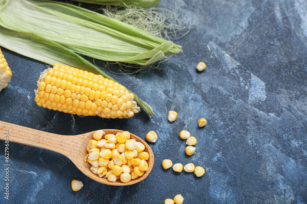 Fresh corn cobs and wooden spoon with kernels on blue table