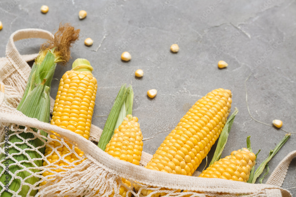 Mesh bag with fresh corn cobs on grey table