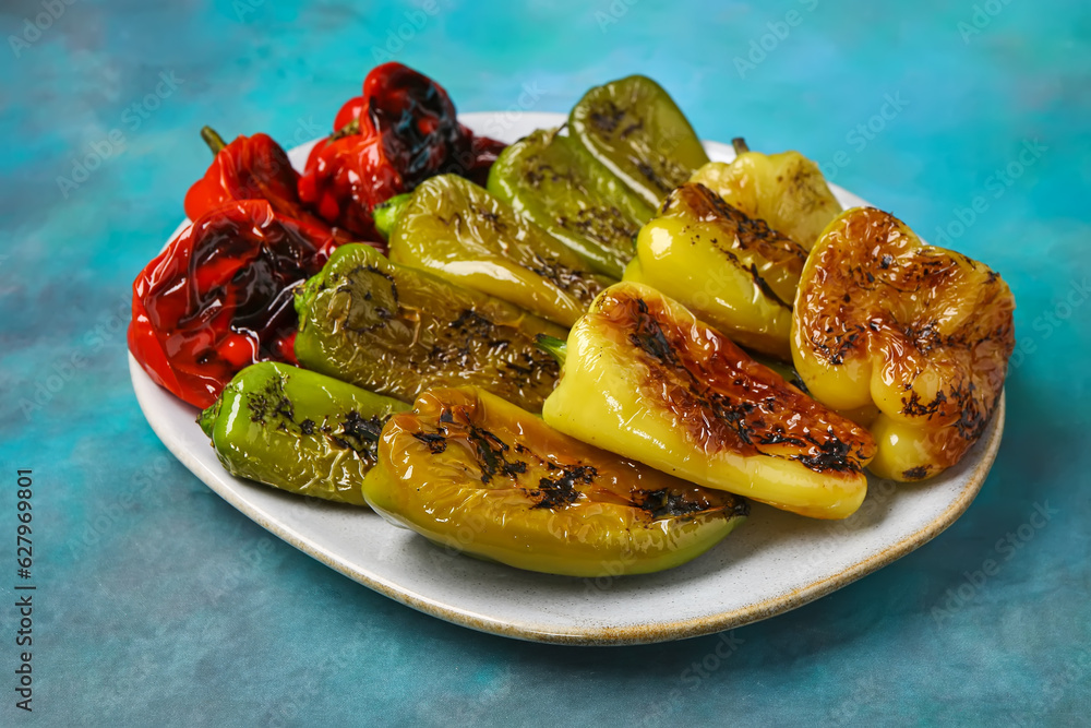 Plate with different grilled peppers on blue background