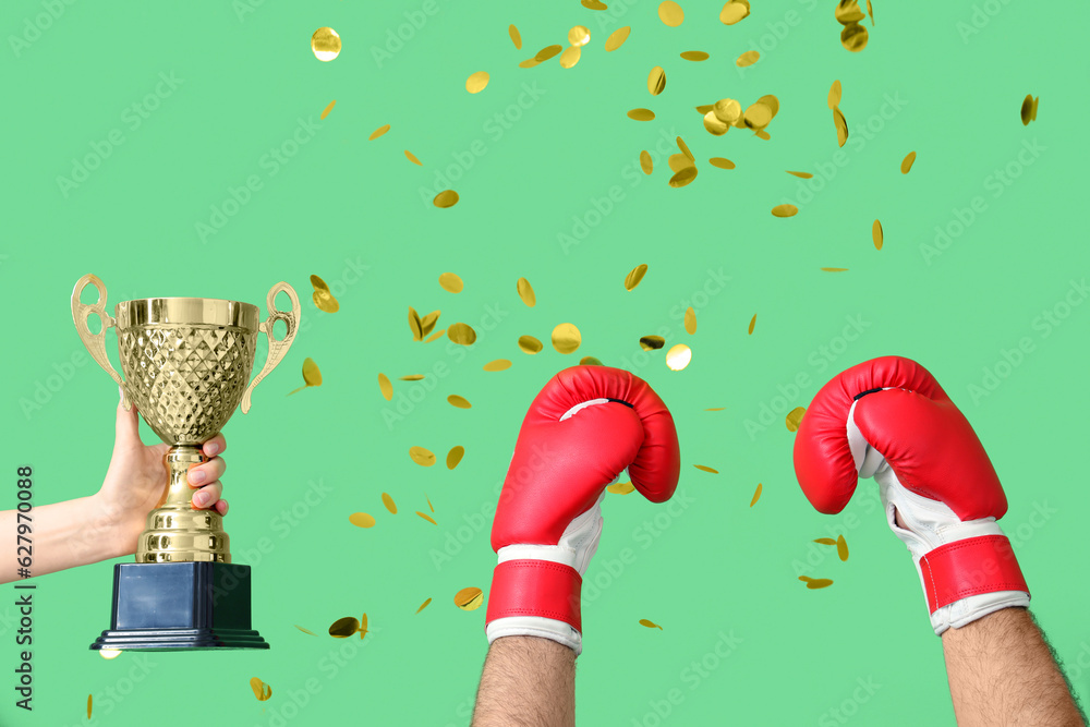 Female hand with gold cup, male hands in boxing gloves and confetti on green background