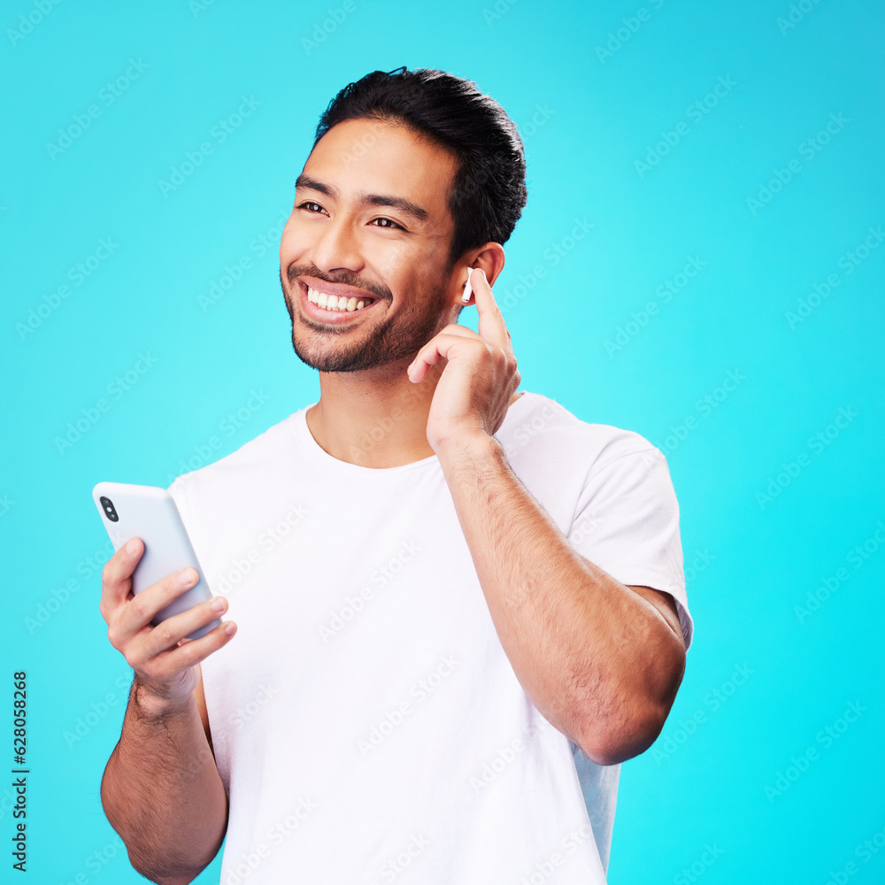 Asian man, earphones and smartphone in studio for music, podcast app and blue background. Happy male