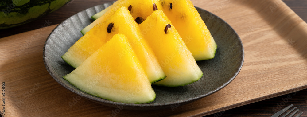 Sliced yellow watermelon in a plate on wooden table background.