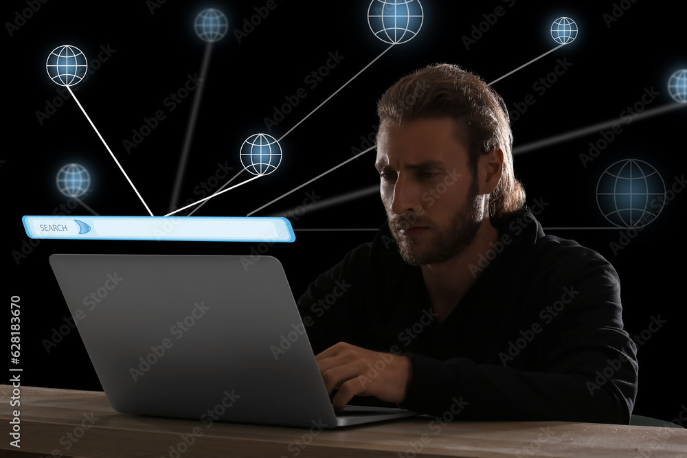 Young man with laptop using web search engine on dark background