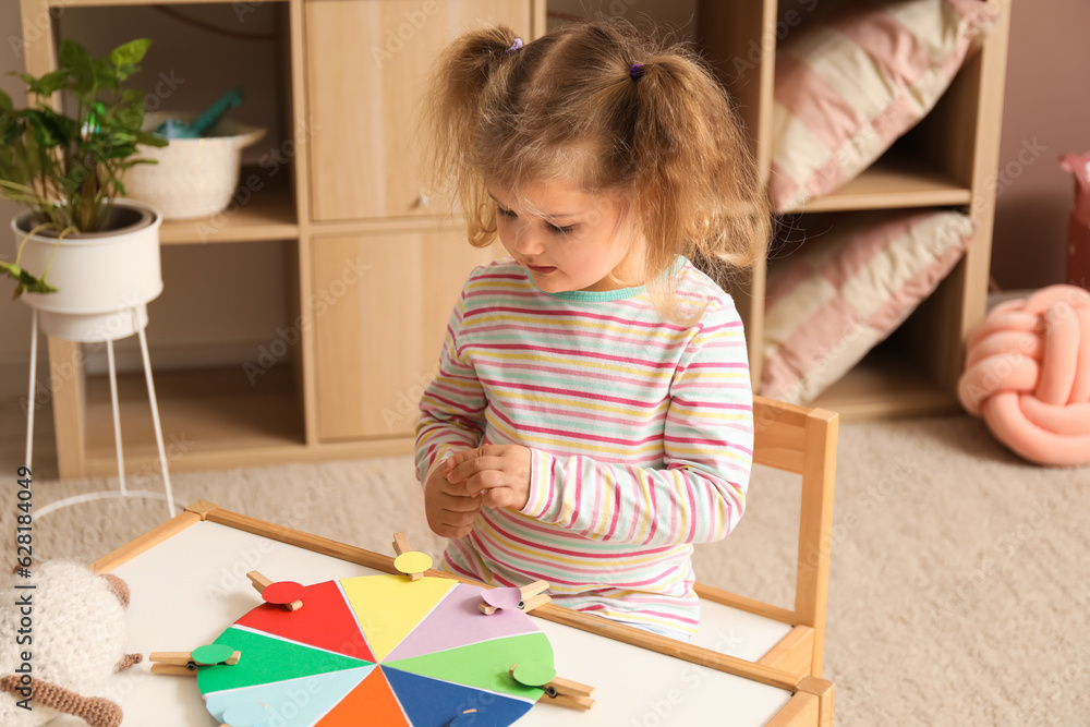 Cute little girl playing matching game with clothespins at home