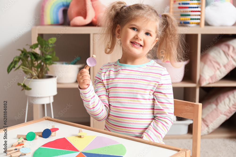 Cute little girl playing matching game with clothespins at home