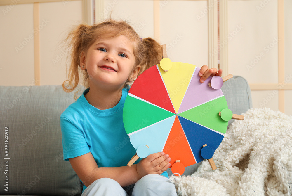 Cute little girl with matching game sitting on sofa at home