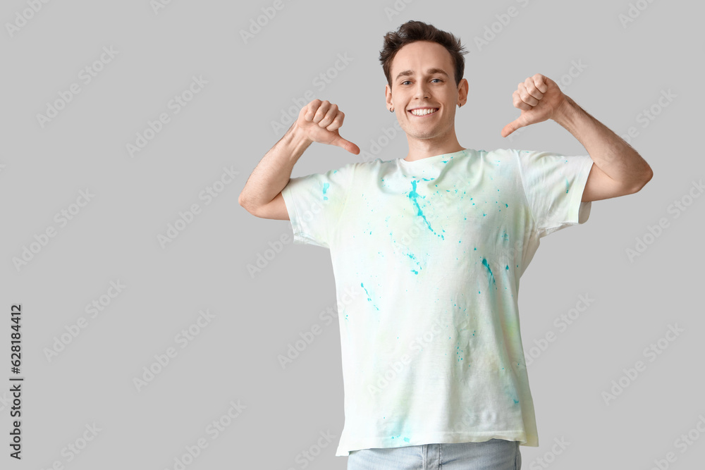 Young man pointing at tie-dye t-shirt on light background