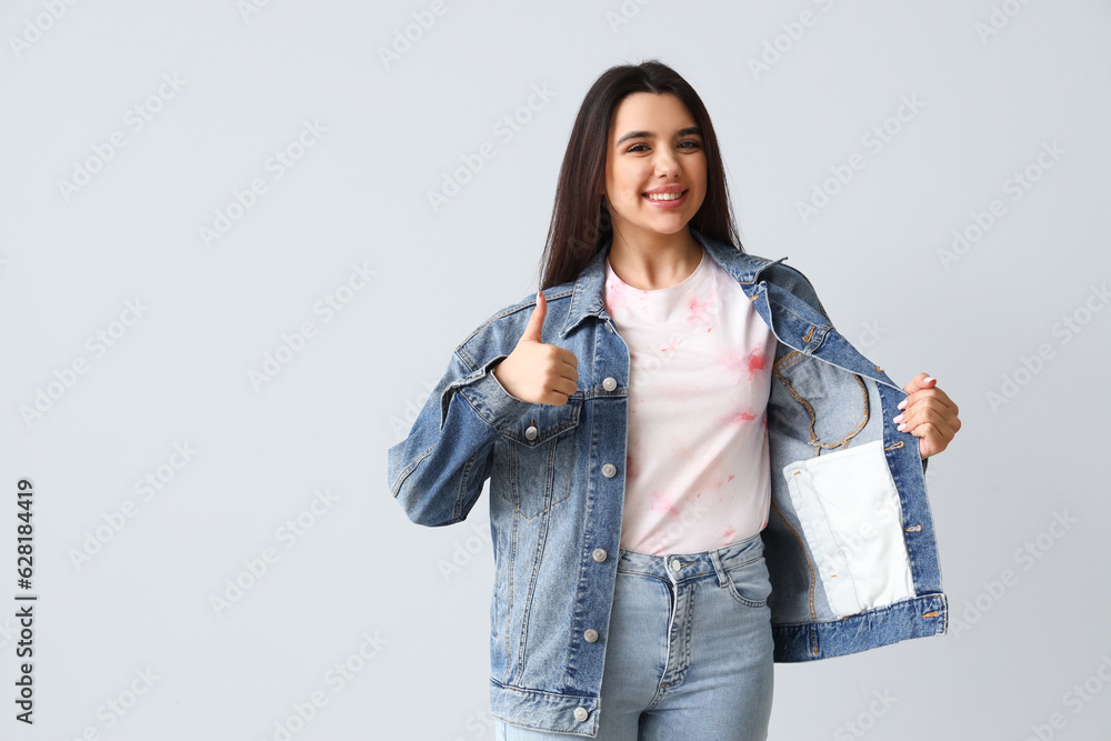 Young woman in tie-dye t-shirt showing thumb-up on light background