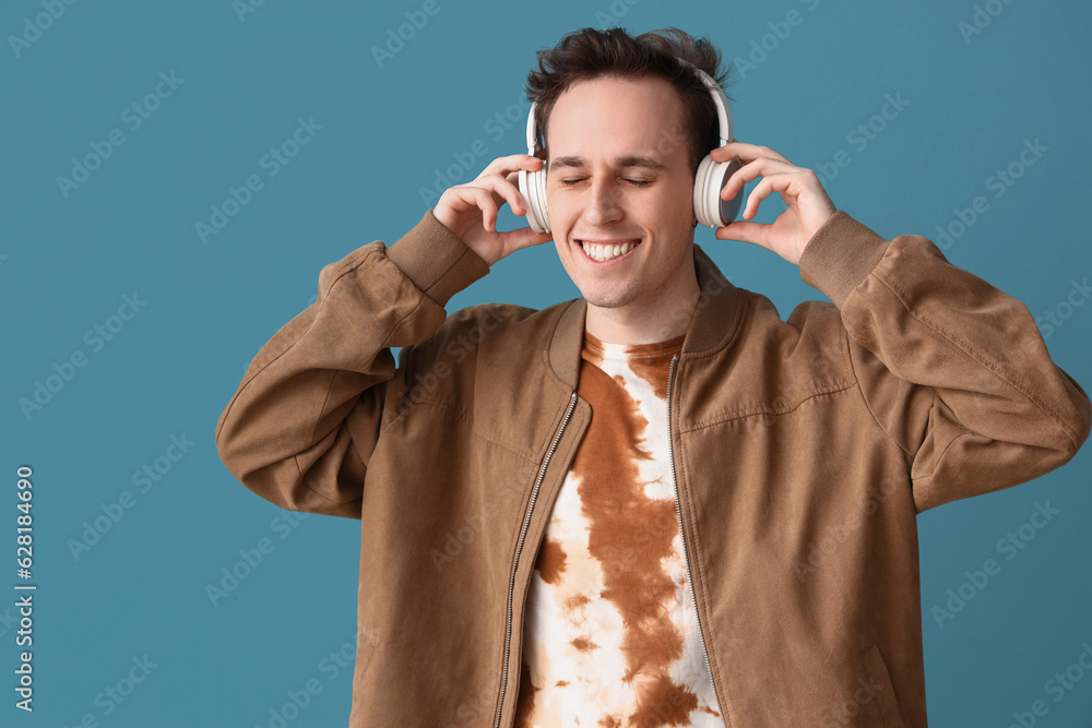 Young man in headphones and tie-dye t-shirt on blue background