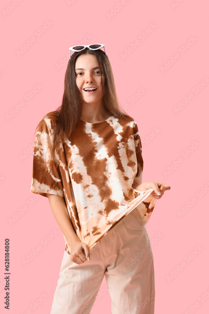 Stylish young woman in tie-dye t-shirt on pink background