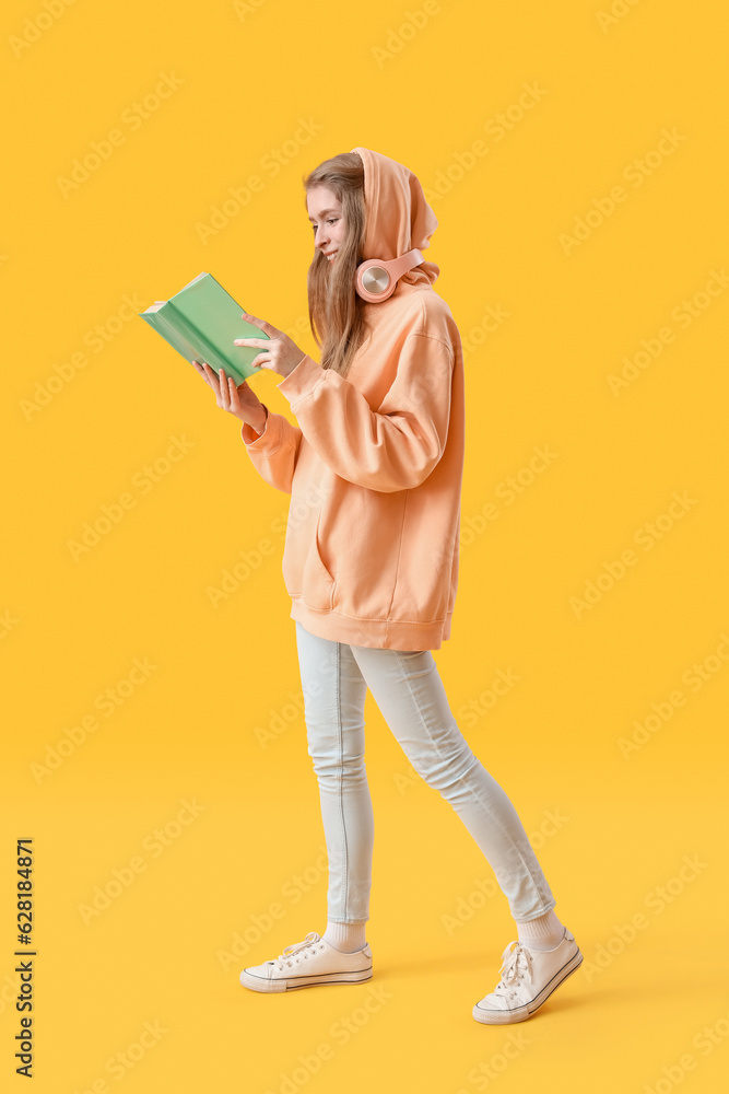 Young woman reading book on yellow background