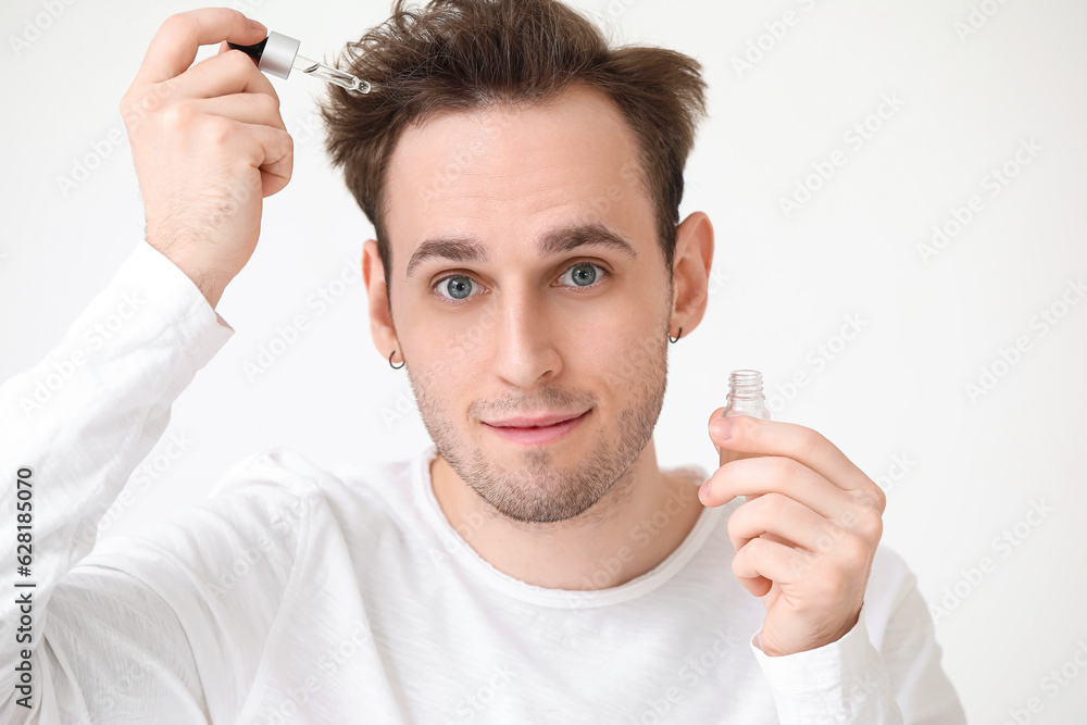 Young man with serum for hair growth on white background, closeup