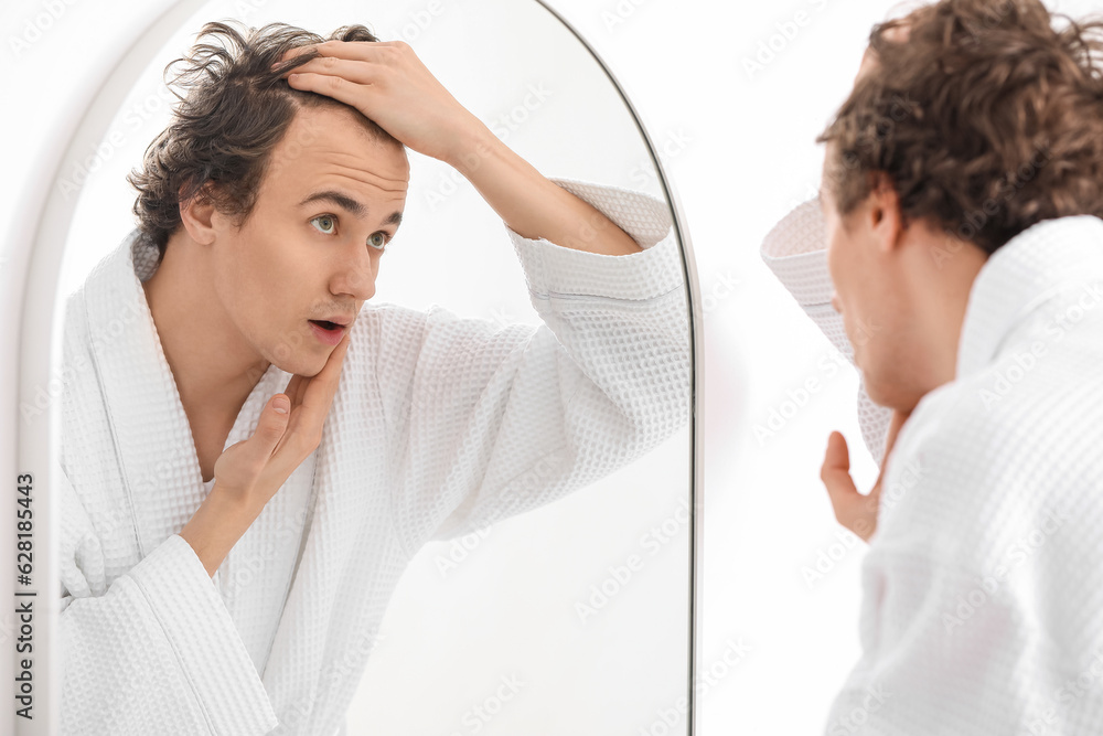 Young man with hair loss problem near mirror in bathroom