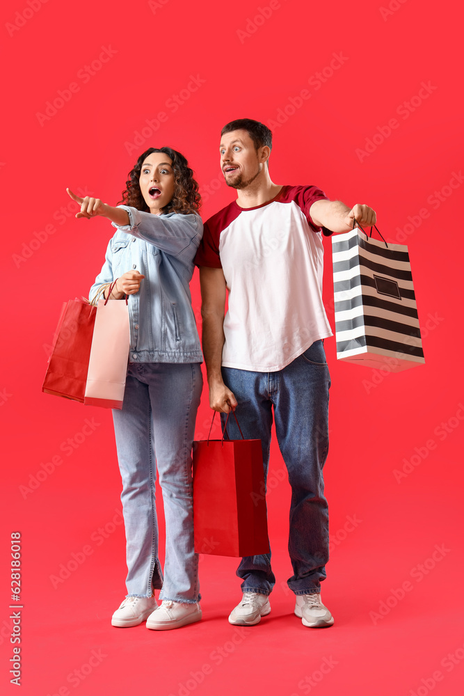 Surprised young couple with shopping bags on red background