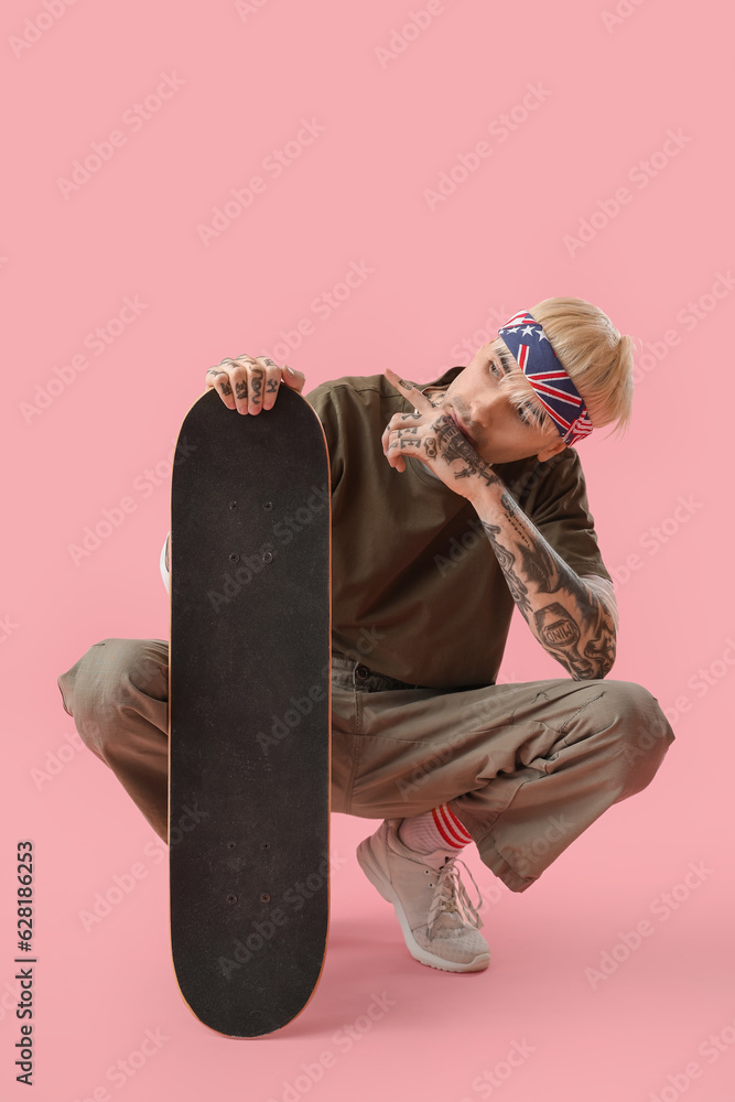 Tattooed young man with skateboard on pink background