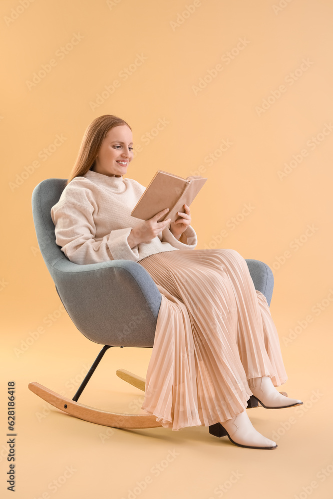 Young woman reading book in armchair on beige background