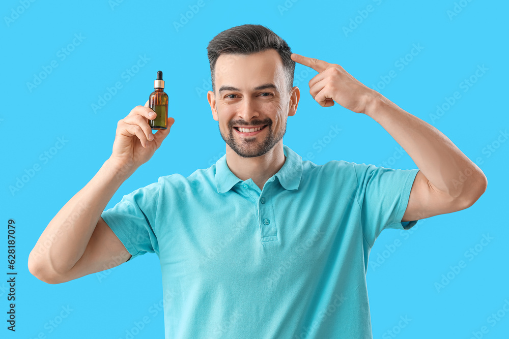 Handsome man with serum for hair growth on blue background