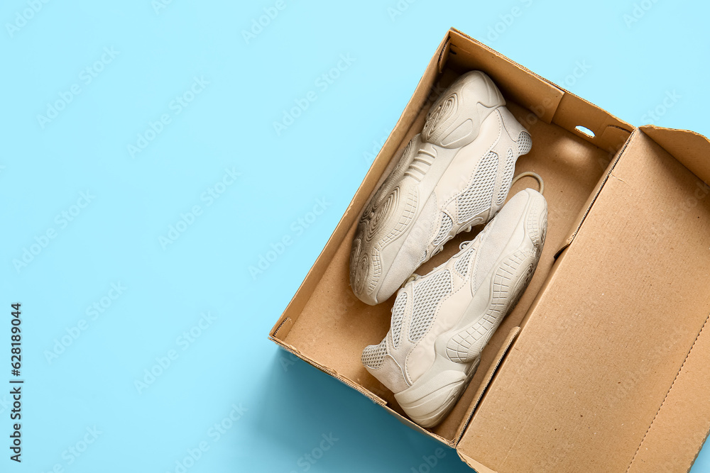 Cardboard box with sports shoes on light blue background