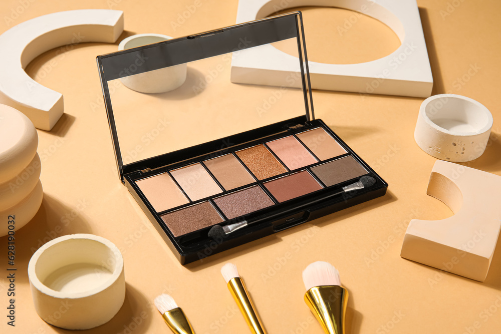 Palette of eyeshadows with brushes and podiums on beige background