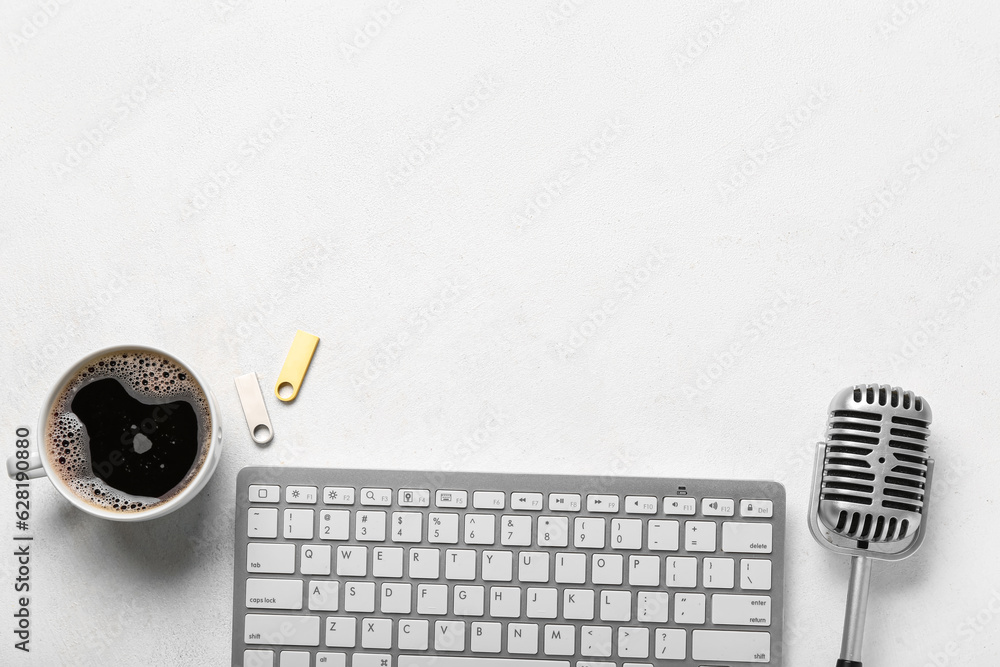 Computer keyboard with USB flash drives, microphone and cup of coffee on white background