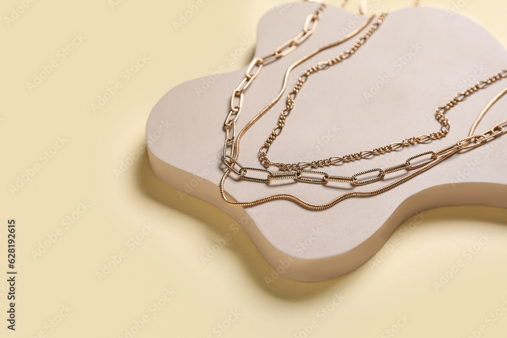 Showcase pedestal with golden necklaces on beige background, closeup