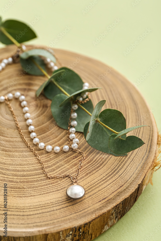 Wooden stand with pearl necklace and eucalyptus branch on green background, closeup