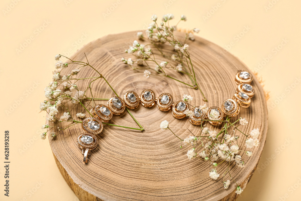 Wooden stand with golden bracelet and flowers on yellow background, closeup