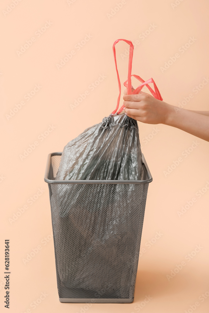 Female hands taking full garbage bag from trash bin on beige background