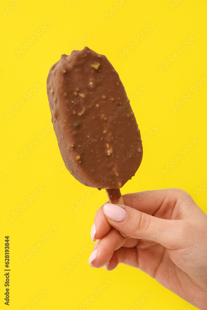 Woman holding delicious chocolate covered ice cream on stick against yellow background