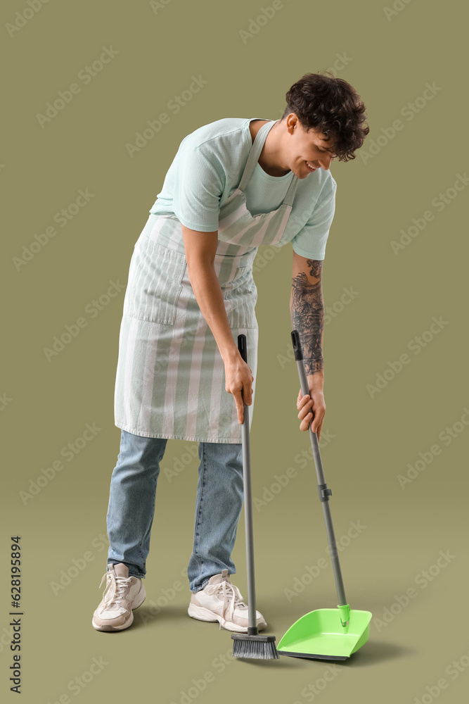 Young man with broom and dustpan on green background