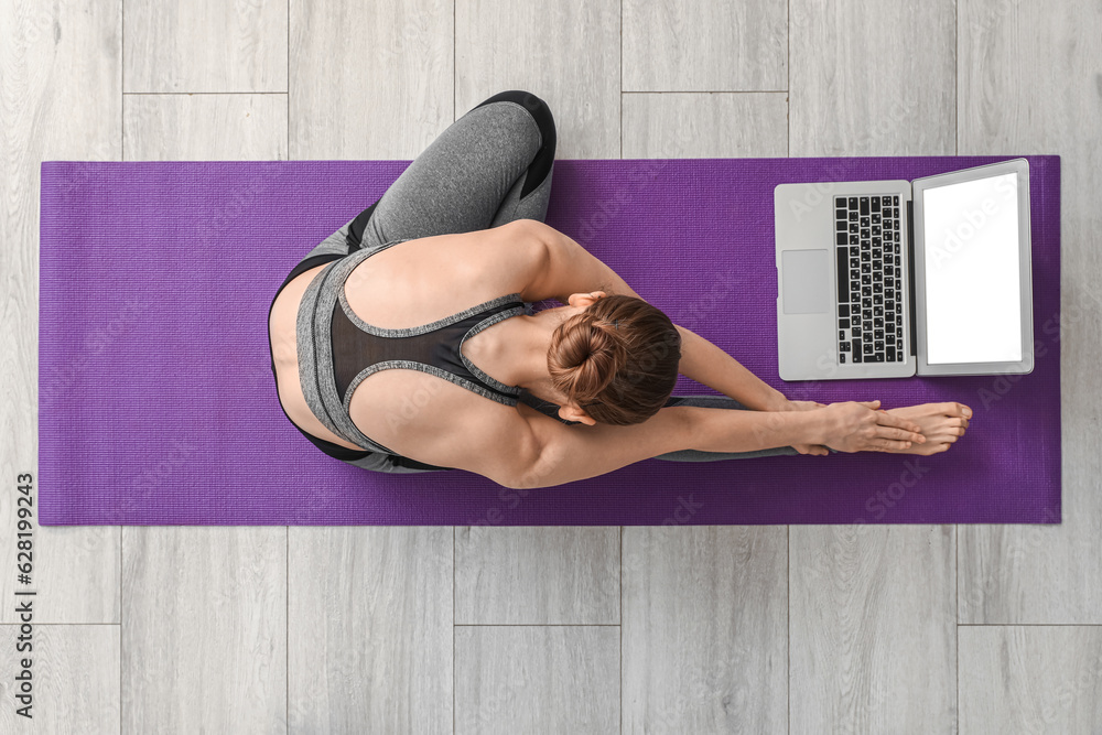 Sporty young woman with laptop doing yoga in gym, top view