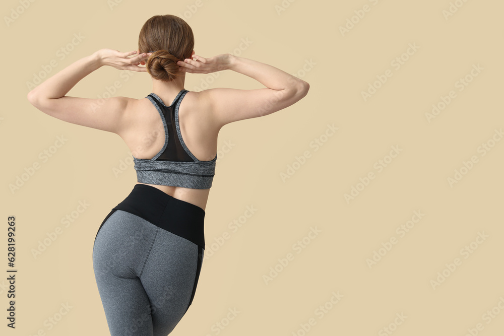 Young woman in sportswear on beige background, back view