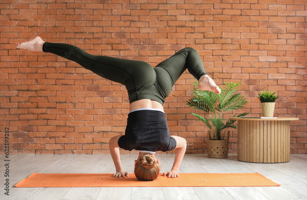 Sporty young woman doing headstand while practicing yoga  at home