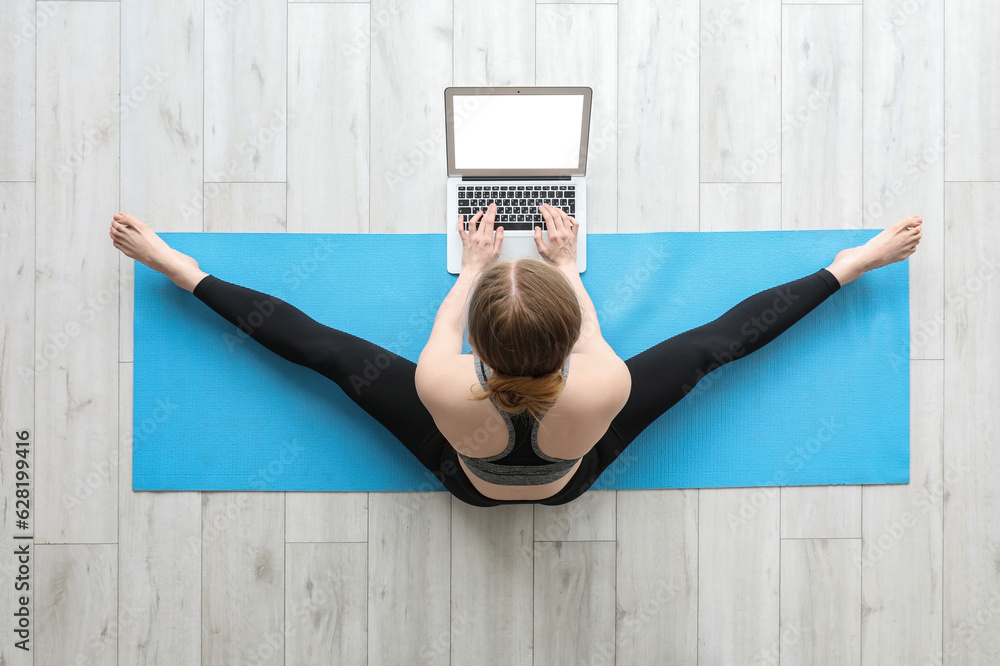 Sporty young woman with laptop doing yoga in gym, top view