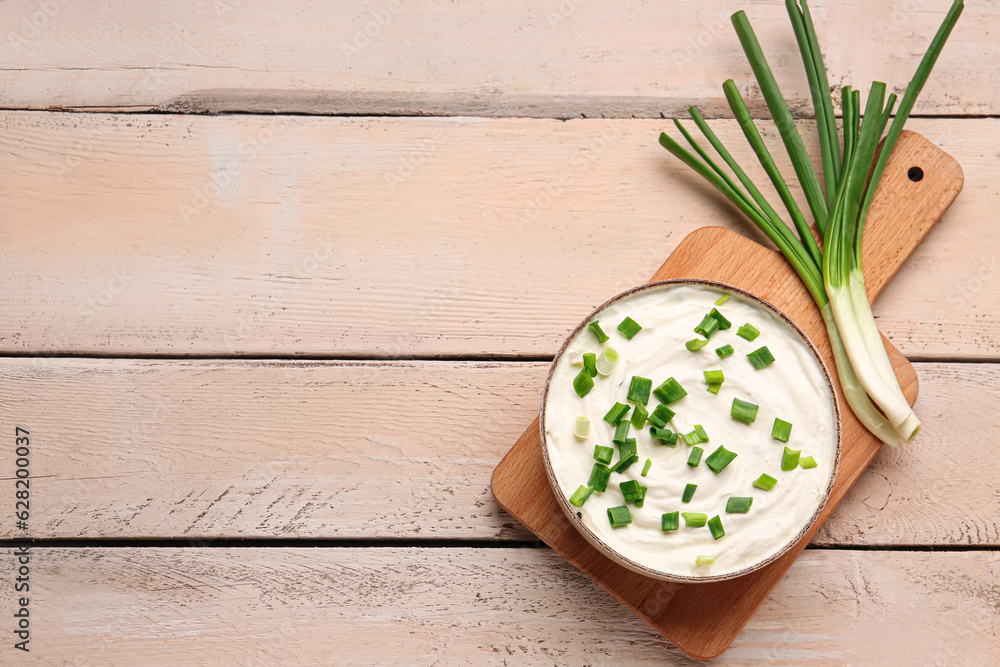 Bowl of tasty sour cream with green onion on light wooden background