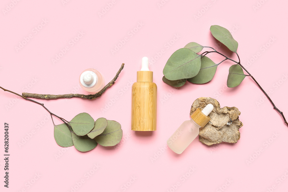 Bottles with cosmetic oil and eucalyptus branch on pink background