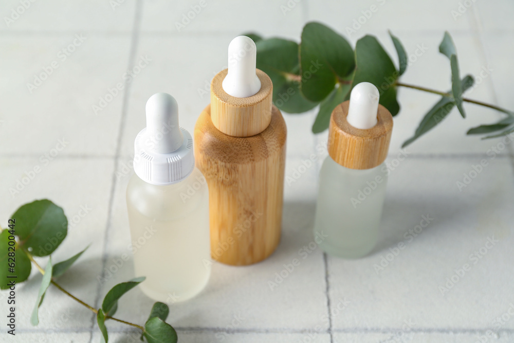 Bottles of cosmetic oil and eucalyptus branches on white tile