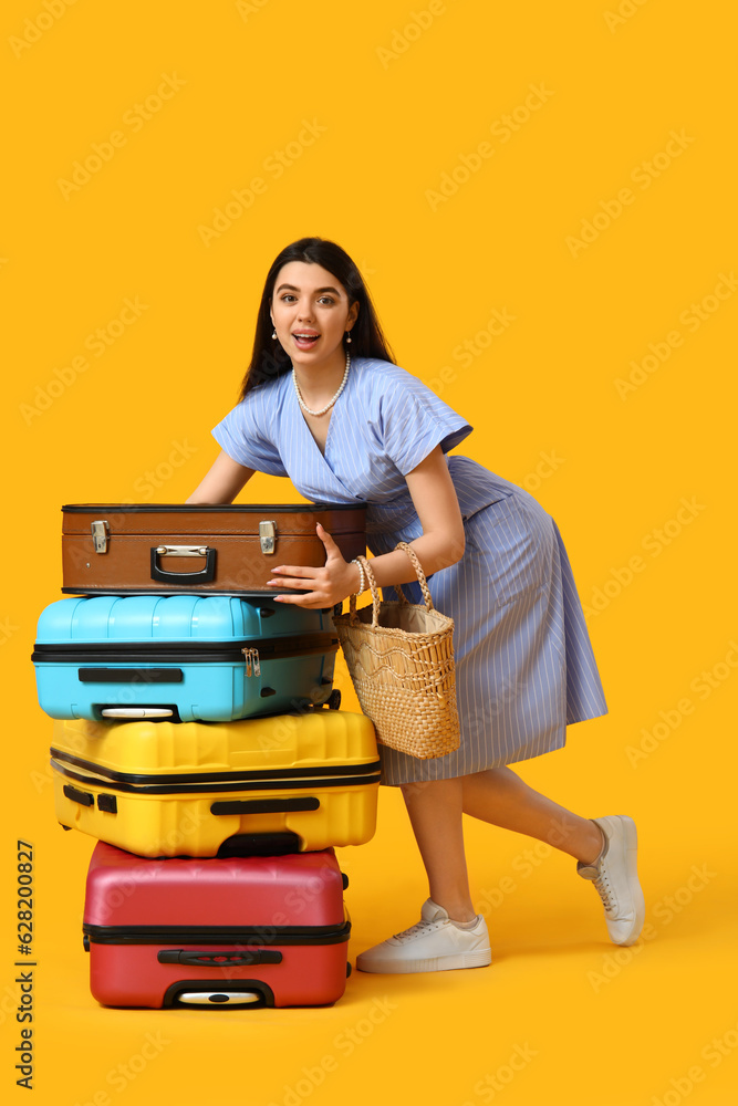 Young woman with suitcases on yellow background