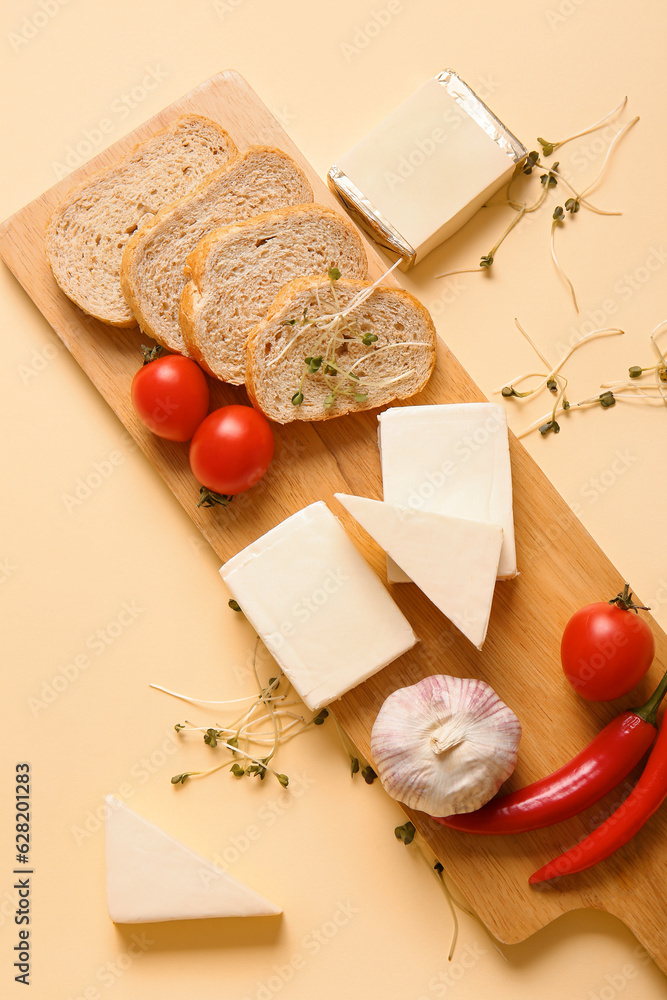 Board with processed cheese, bread and vegetables on pale yellow background