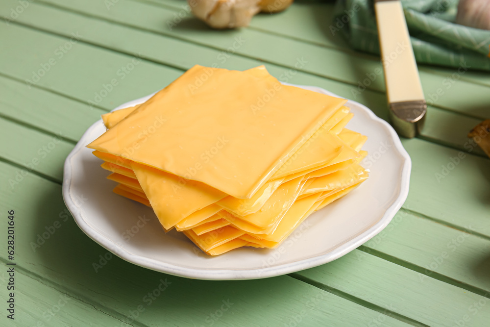 Plate with slices of tasty processed cheese on green wooden background