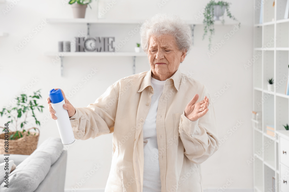 Displeased senior woman with air freshener at home