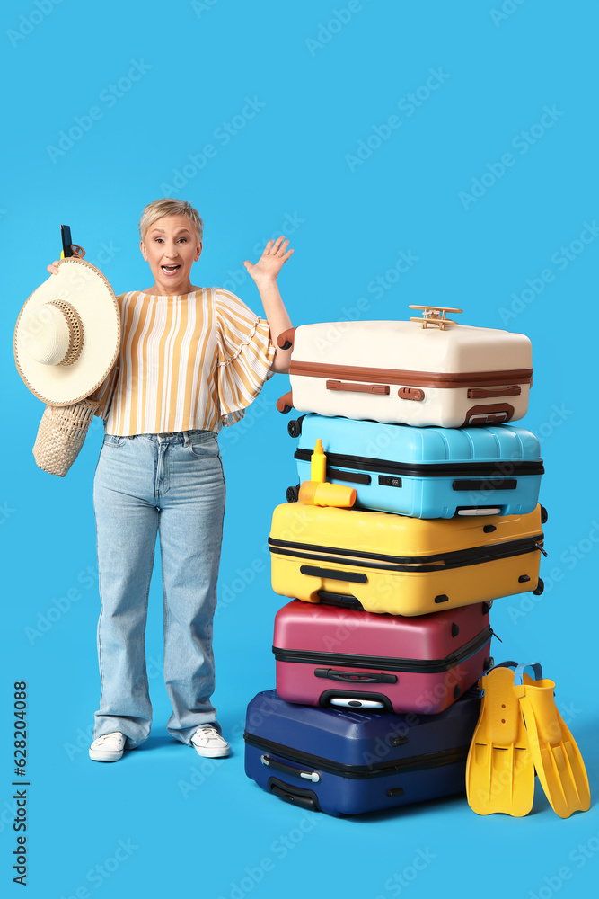 Mature woman with suitcases and beach accessories on blue background