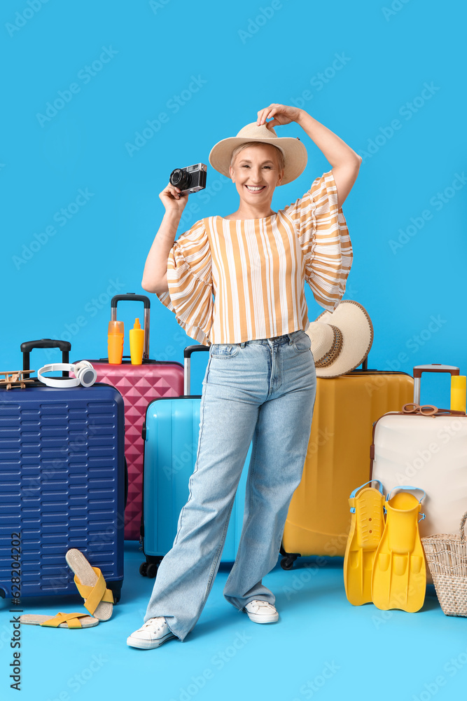 Mature woman with photo camera and suitcases on blue background