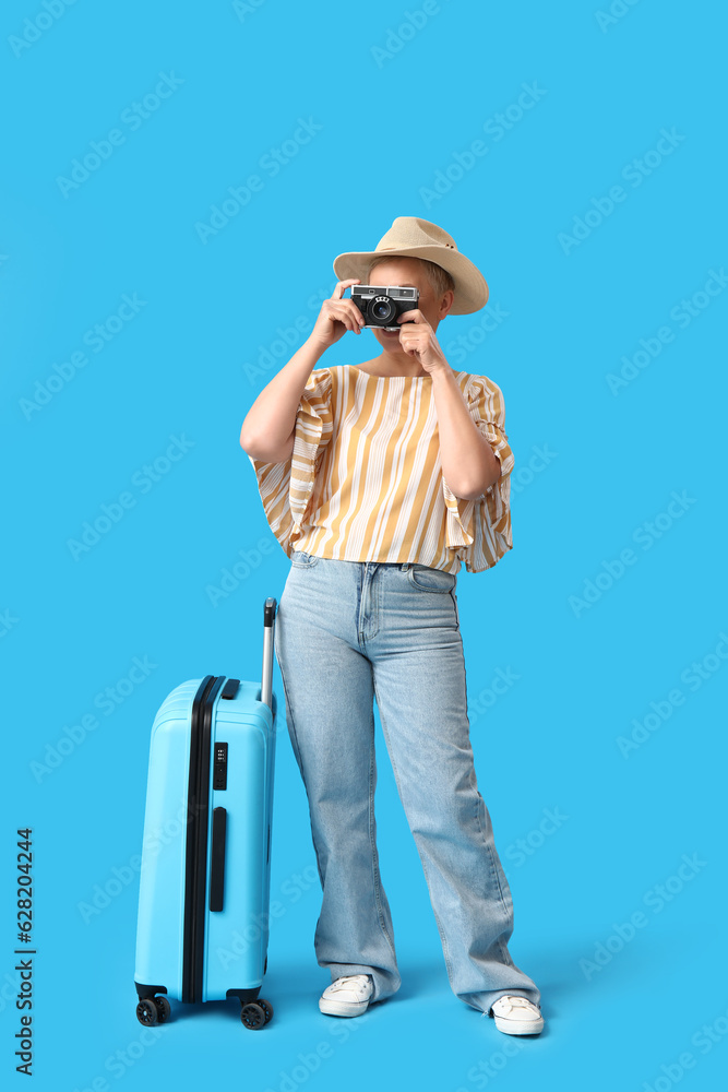 Mature woman with photo camera and suitcase on blue background