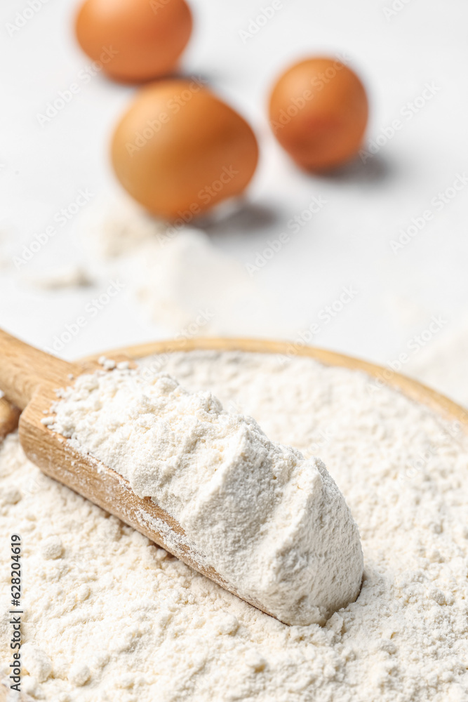 Wooden bowl with wheat flour, scoop and eggs on white background