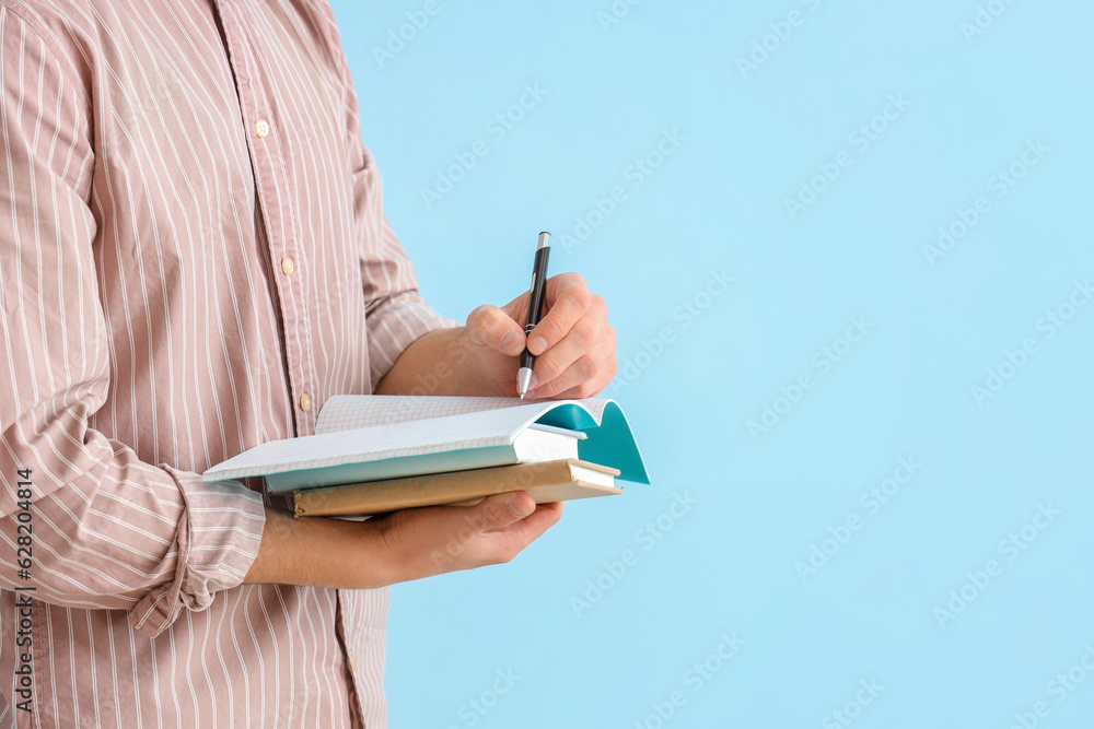 Male student writing in notebook on blue background