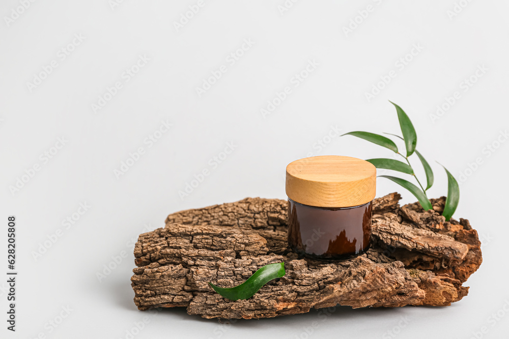 Jar of cosmetic product, tree bark and plant leaves on light background