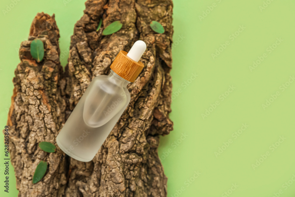 Bottle of essential oil, tree bark and plant leaves on green background, closeup