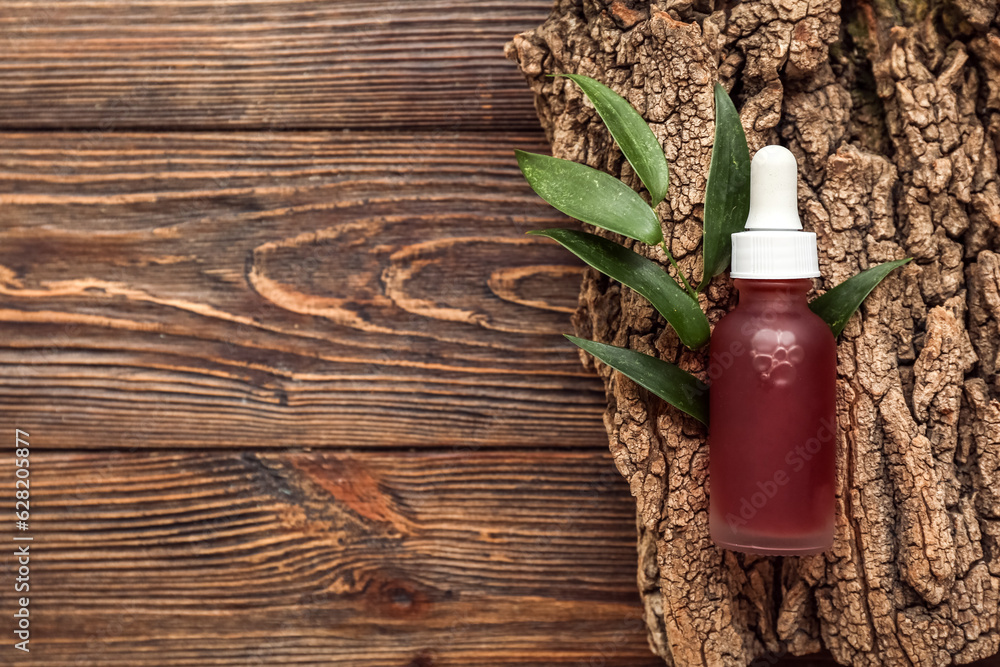 Bottle of essential oil, tree bark and plant leaf on wooden background, closeup