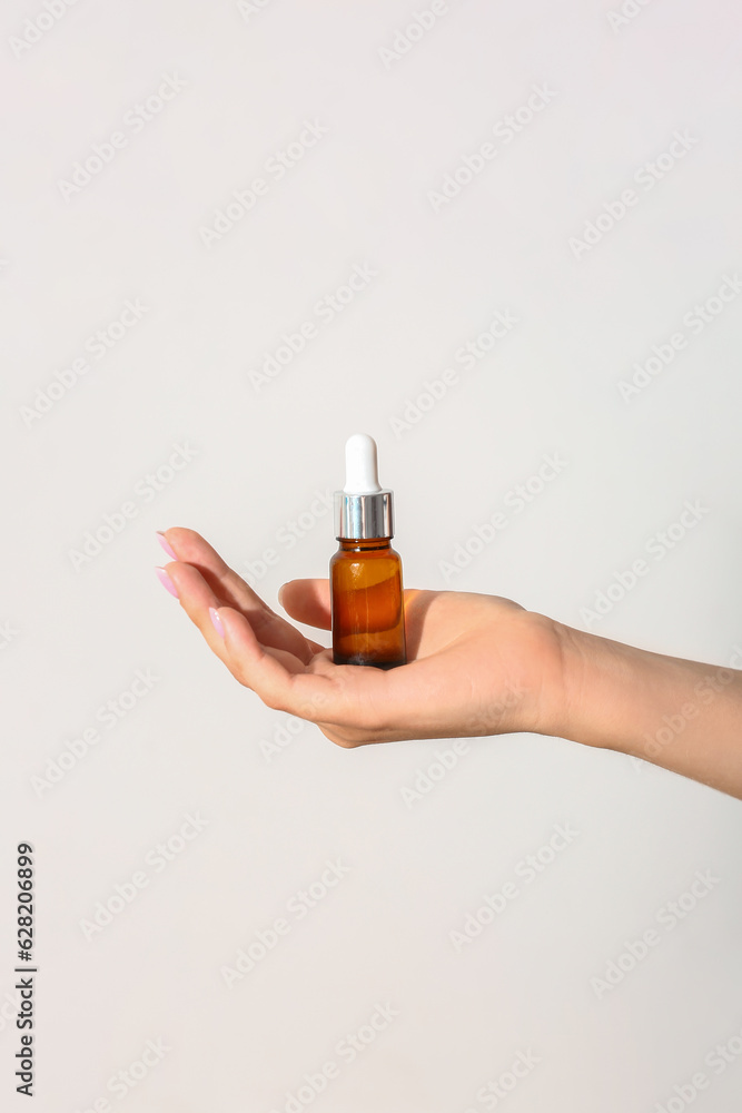 Hand of woman with bottle of cosmetic oil on light background